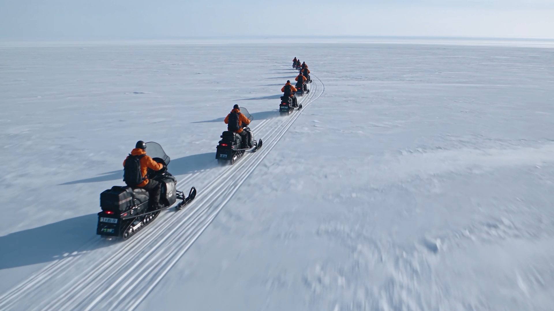 A convoy of snowmobiles crossing a vast white ice field, from the Amersia reel